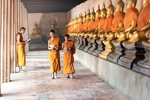 Bildmittelpunkt: Drei junge buddhistische Mönche in einem Kloster in Kambodscha | rechts: lange Reihe mit Budda-Statuen